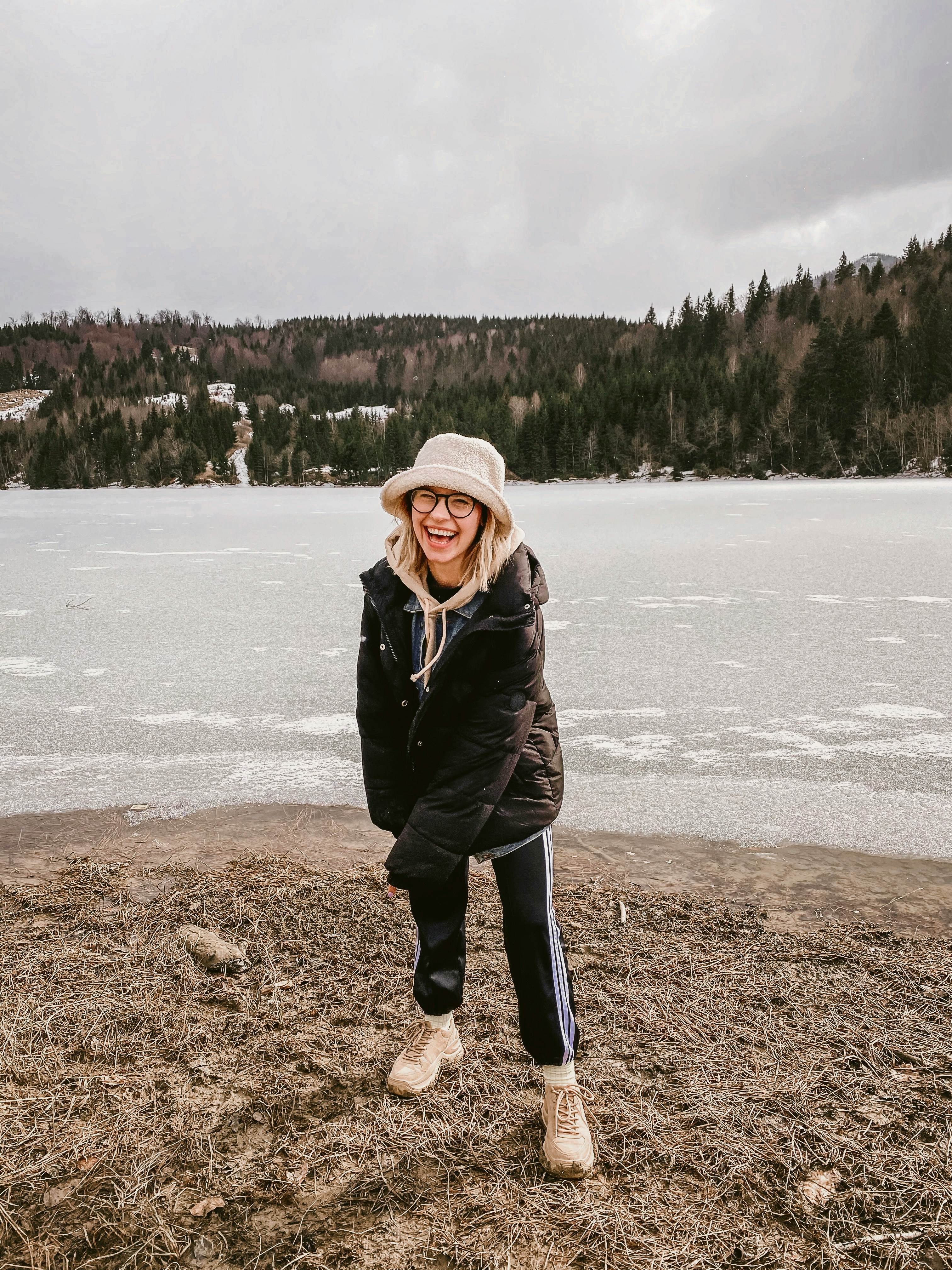 a woman standing by a small lake, she has a playful and genuine smile